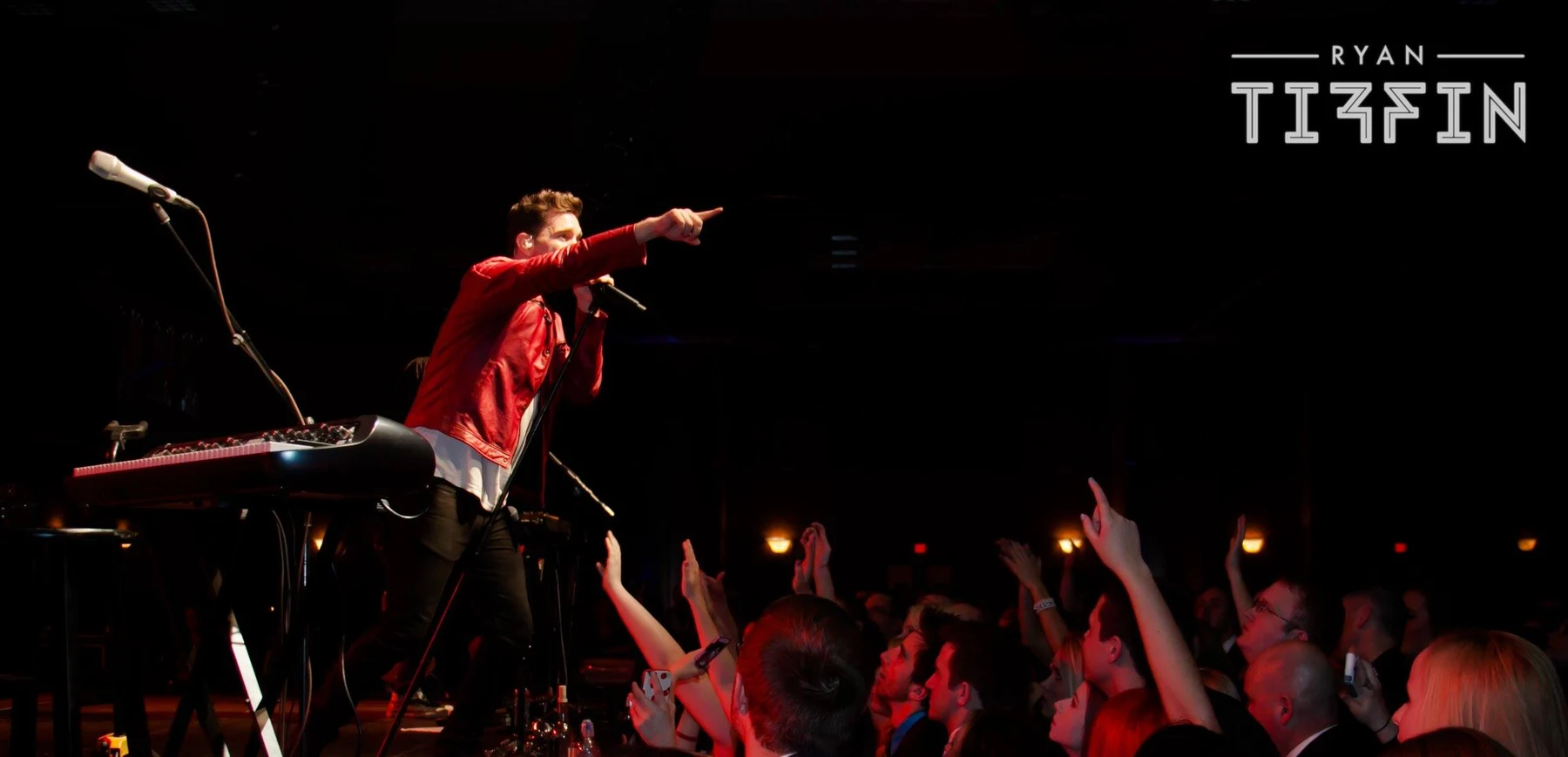 Live-performance photograph of a musician engaging an audience from the stage