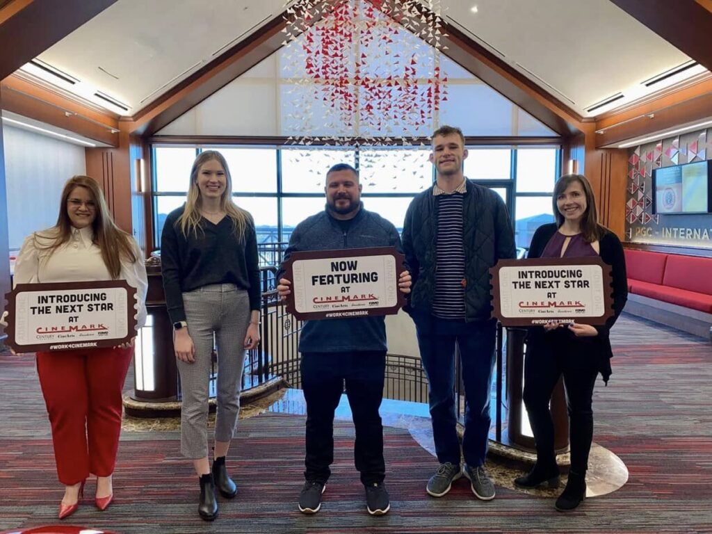 A group of cinema team members standing together at a workplace recognition event, reinforcing the importance of employee experience and trust.